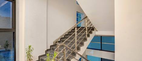 Un escalier moderne avec des rampes en métal, des plantes en pot et une vue sur l’extérieur grâce à une grande fenêtre.