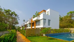 Un edificio residencial moderno con piscina, rodeado de abundante vegetación y una valla de madera.