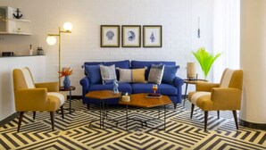 Una sala moderna con un sofá azul, dos sillones, una mesita de centro y un suelo estampado. Hay cuadros enmarcados en la pared y una lámpara.