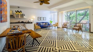 Una sala de estar moderna con piso de diseño geométrico, un comedor con mobiliario de madera y ventanas amplias que ofrecen vistas a árboles.