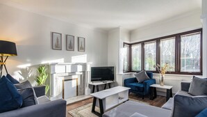 Ένα μοντέρνο σαλόνι με γκρι καναπέδες, μια τηλεόραση επίπεδης οθόνης, ένα τζάκι και μεγάλα παράθυρα με περσίδες.