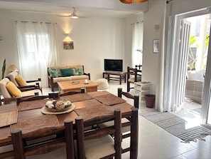 A living room with a sofa, TV, coffee table, and dining area with chairs and a table.