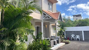 A two-story house with a covered porch, outdoor seating, and lush greenery. - Tropical 3-bedroom villa 5 min from the beach, perfect for families (Flic en Flac)