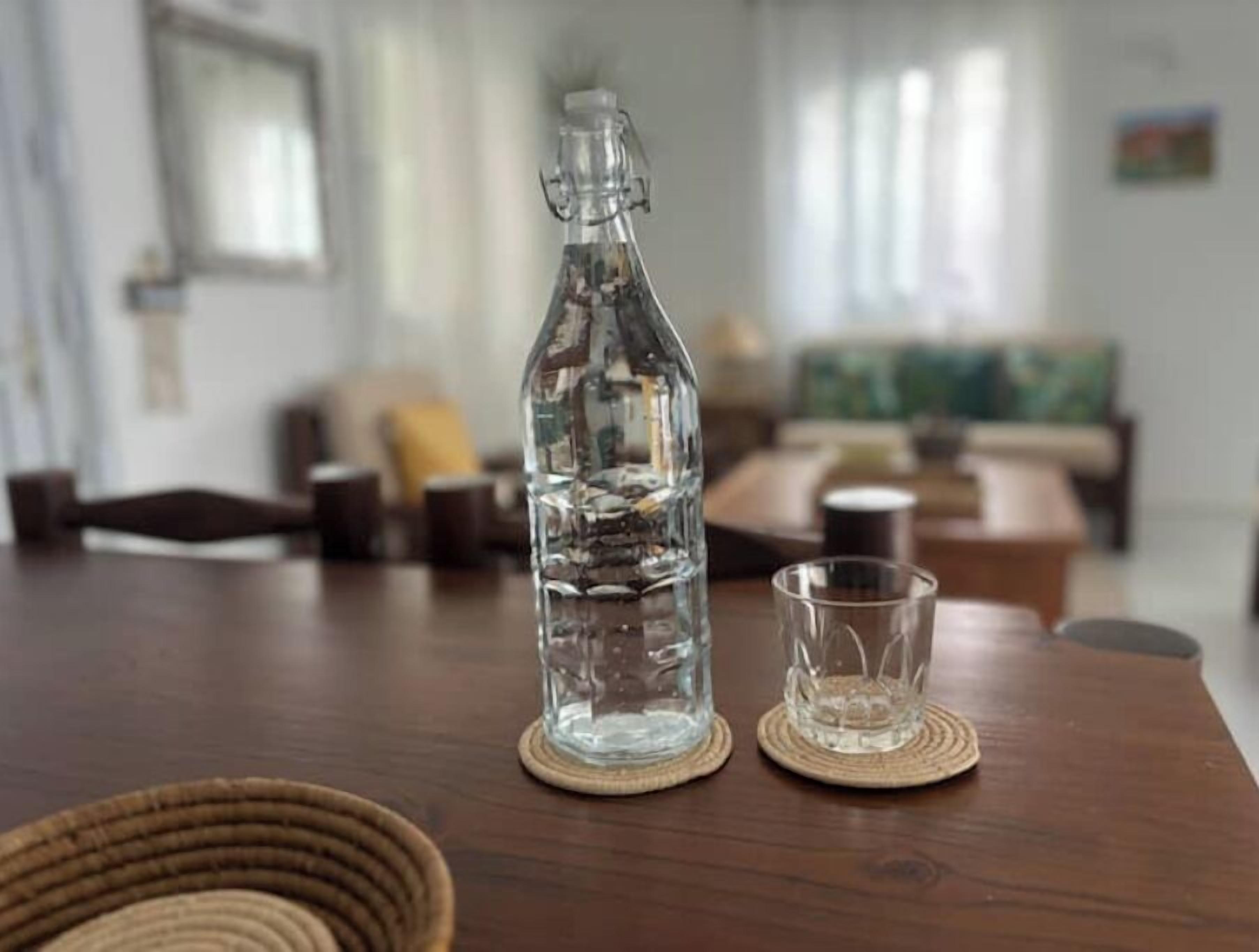A clear bottle of water on a wooden table with a coaster, a glass, and a woven basket.