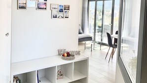 A modern living room with a white console table, bookshelves, and a large window offering a city view. - Comfy Vista Apartment (Kalamata)