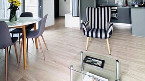 A modern living space with a dining area, a striped armchair, and a kitchen with dark cabinets and a stainless steel refrigerator. - Comfy Vista Apartment (Kalamata)