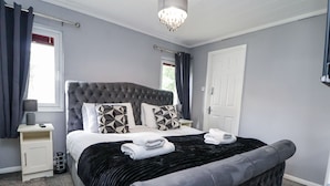 A modern bedroom with a tufted headboard, a large bed with geometric patterned pillows, a black velvet throw, and a white door. - 155 Woodland Hall (Ruthin)