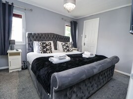 Un dormitorio moderno con cabecera capitonada, una cama grande con almohadas de estampado geométrico, un plaid de terciopelo negro y una puerta blanca.