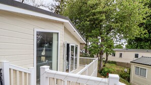 A mobile home with a white exterior, a deck with white railings, and a large tree in the background. - 155 Woodland Hall (Ruthin)