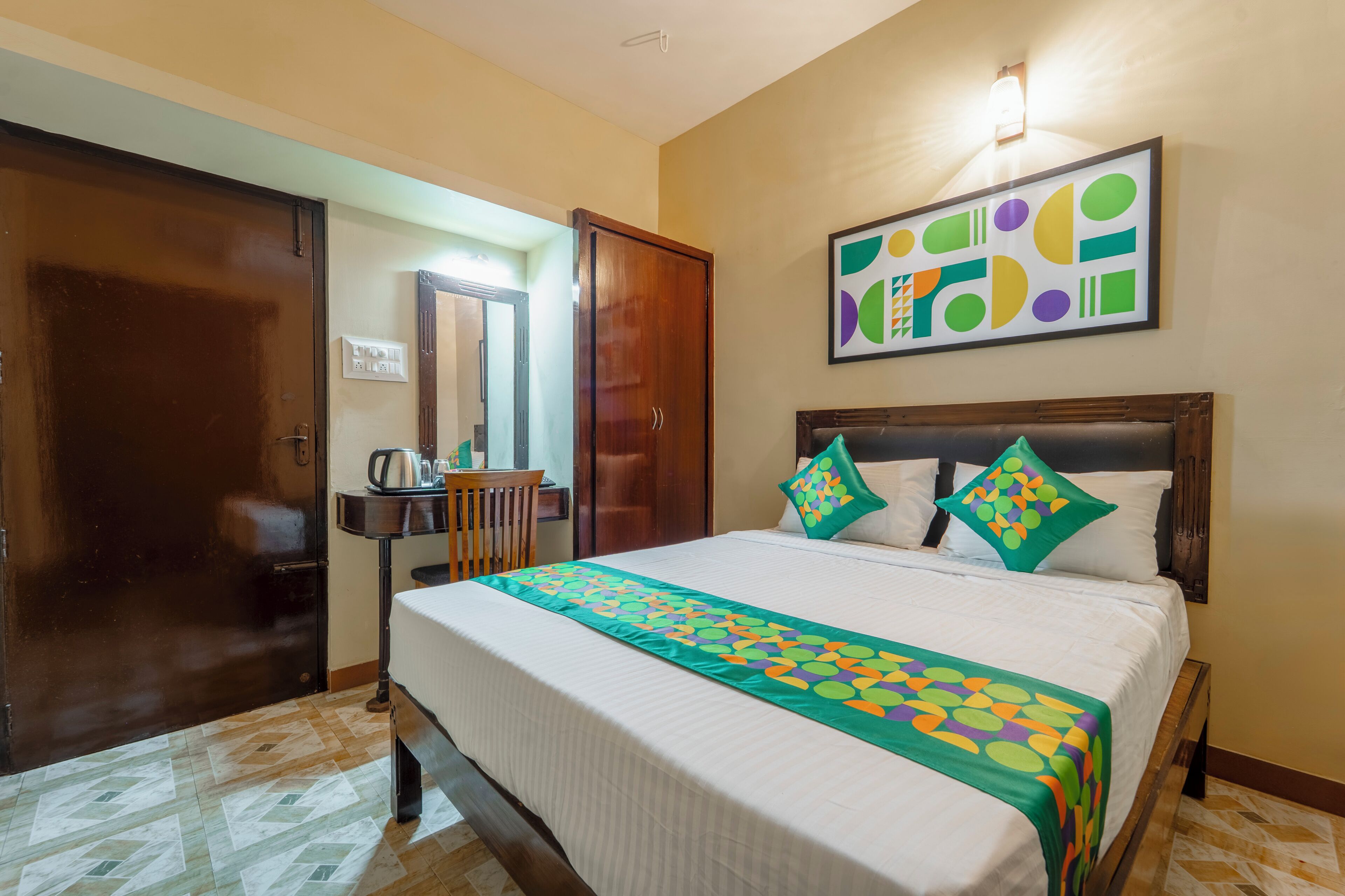 Une chambre d’hôtel comprenant un lit, une armoire en bois, un bureau avec une chaise et un luminaire fixé au mur.