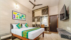 Quarto de hotel com cama, ventoinha no teto, televisão presa na parede, banheiro com espelho e porta.
