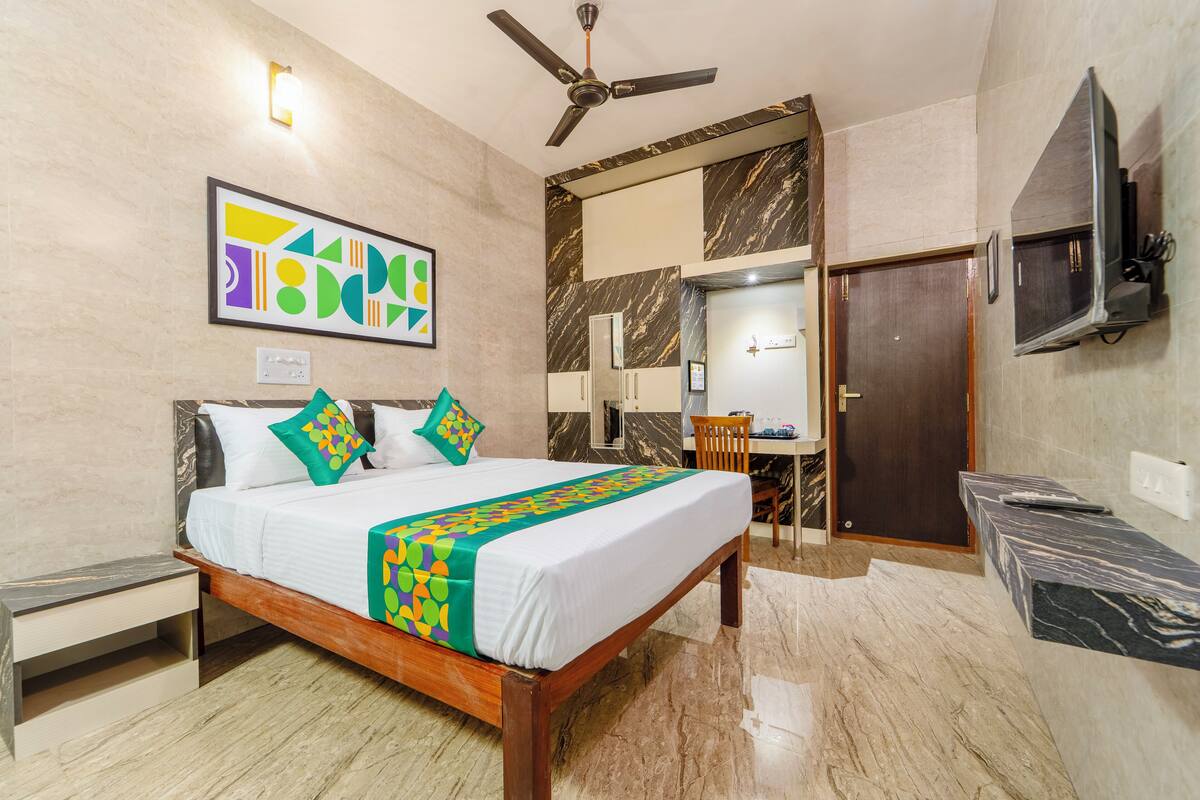 Une chambre d’hôtel avec un lit, un ventilateur de plafond, un téléviseur fixé au mur, une salle de bain avec un miroir et une porte.