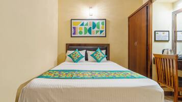 Una cama bien tendida con una colcha estampada y dos almohadas decorativas, una obra de arte abstracta enmarcada en la pared y un armario de madera.