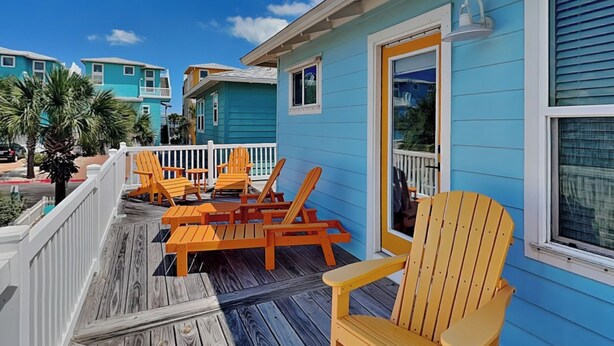 A wooden deck with outdoor seating and a view of a blue building.