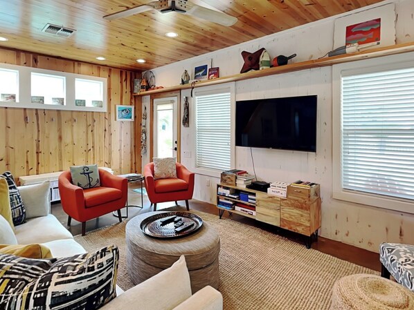 A cozy living room with wooden walls and ceiling, two red armchairs, a white sofa, a coffee table, and a TV mounted on the wall.