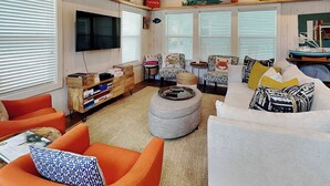 A cozy living room with a wooden ceiling, a television, and a variety of seating including an orange armchair and a white sofa.
