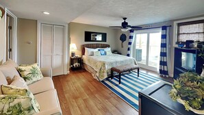 Un dormitorio con cama, ventilador de techo, televisor, escritorio y ventana con cortinas.