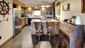Una cocina moderna con una isla central, electrodomésticos de acero inoxidable, armarios de madera y un adorno con forma de timón.
