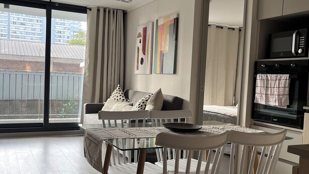 A modern kitchen with a microwave, oven, and dining area with white chairs and a glass table.