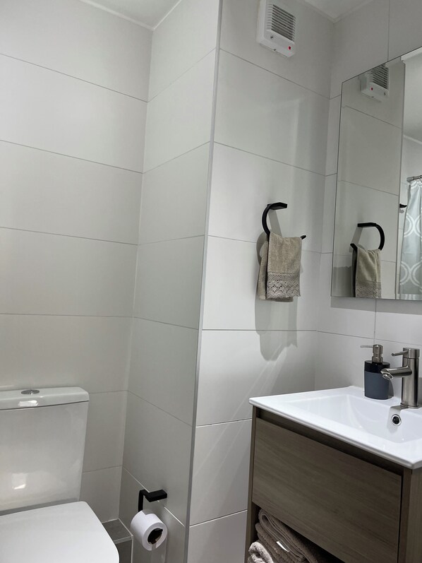 A bathroom with white tiles, a toilet, a sink with a mirror, and two towels hanging on hooks.