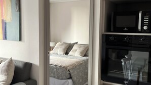 A modern bedroom with a bed, a grey sofa, and a dining area with a table and chairs.
