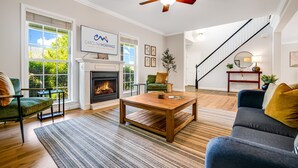 A spacious living room with a fireplace, a television mounted above it, and a staircase leading to another level.