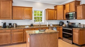 A kitchen with wooden cabinets, granite countertops, a built-in oven, a microwave, and a window with a view of trees.