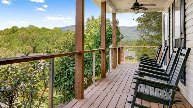 A wooden deck with a ceiling fan, wooden railings, and a view of a forested area.