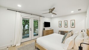A bedroom with a bed, a TV, a ceiling fan, and a window with curtains.