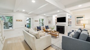 A spacious living room with a fireplace, a flat-screen TV mounted above it, and a large window providing a view of the outdoors.