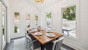 A dining area with a wooden table set for four, white walls, and large windows.