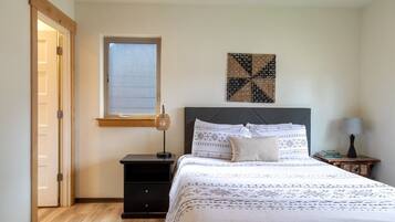 A bedroom with a bed, a nightstand, a lamp, a window, and a door.