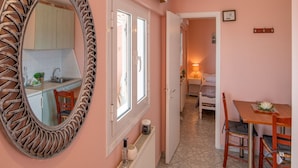 Een compacte kamer met een kitchenette, een eettafel met stoelen, een grote spiegel en een bed in de aangrenzende ruimte.