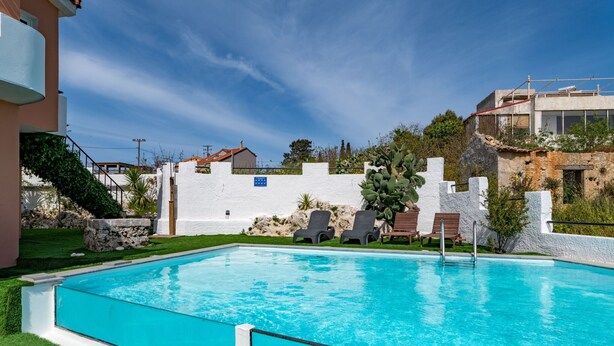 Una piscina rectangular con agua azul cristalina, rodeada por un muro blanco y una zona ajardinada.