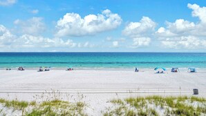 Ein Strand mit weißem Sand, klarem blauen Wasser und einigen Zelten und Sonnenschirmen.