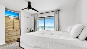 Ein Schlafzimmer mit einem Bett, einem Deckenventilator, einem Kleiderschrank und einem großen Fenster mit Blick auf den Strand.