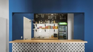 Eine Bar mit blauer Wand, einer Kreidetafel als Speisekarte, Regalen mit Flaschen und einem Kühlschrank.