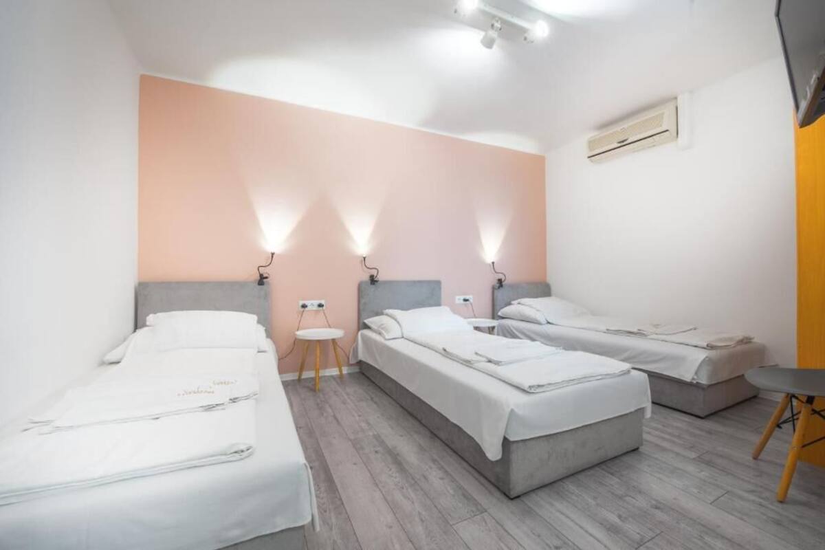A hotel room with three beds, a small table, and wall-mounted lights.