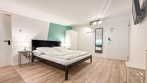 Ein modernes Schlafzimmer mit Holzboden, einem Bett mit weißen Leinen, einem Nachttisch mit Lampe und einem großen Spiegel an der Wand.