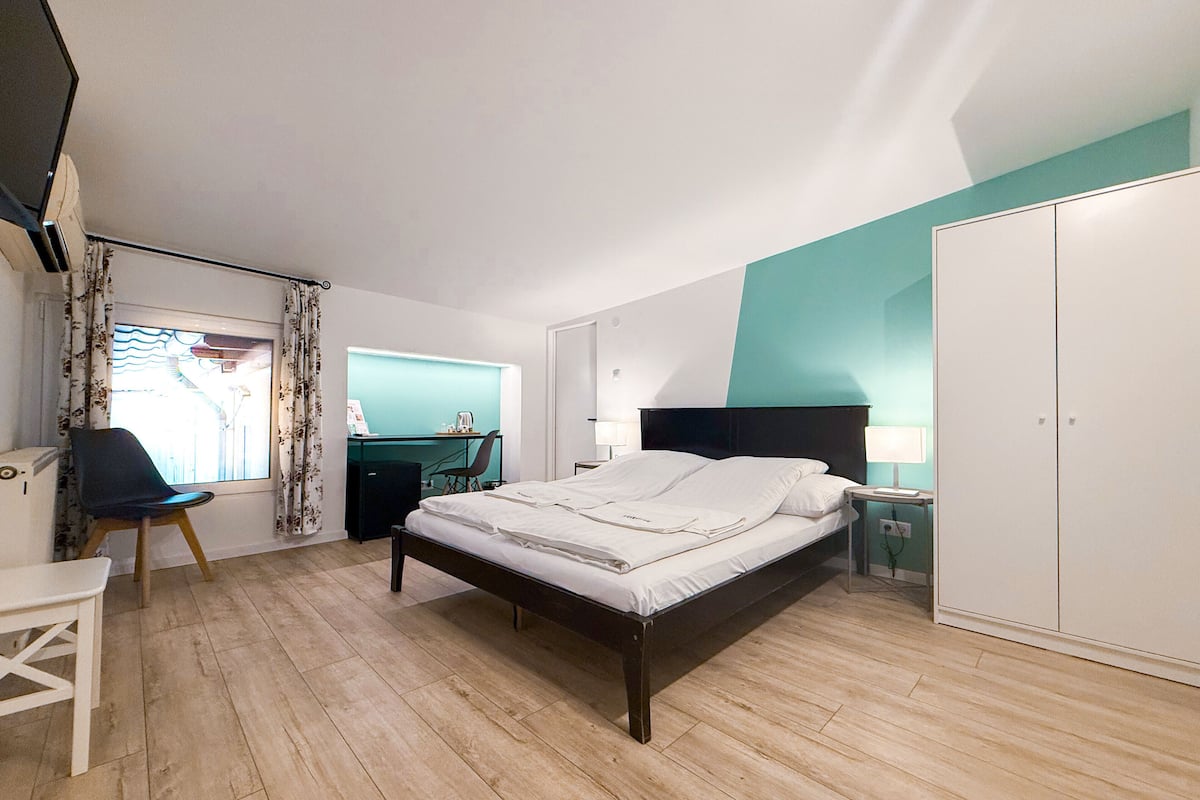 A bedroom with a bed, a desk, a chair, a wardrobe, and a window with curtains.