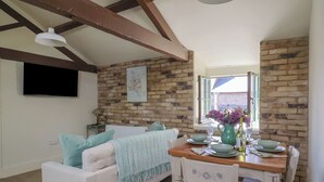 A cozy living room with a white sofa, a wooden dining table set for two, and a brick wall. - Drake's Hideaway (Lyme Regis)