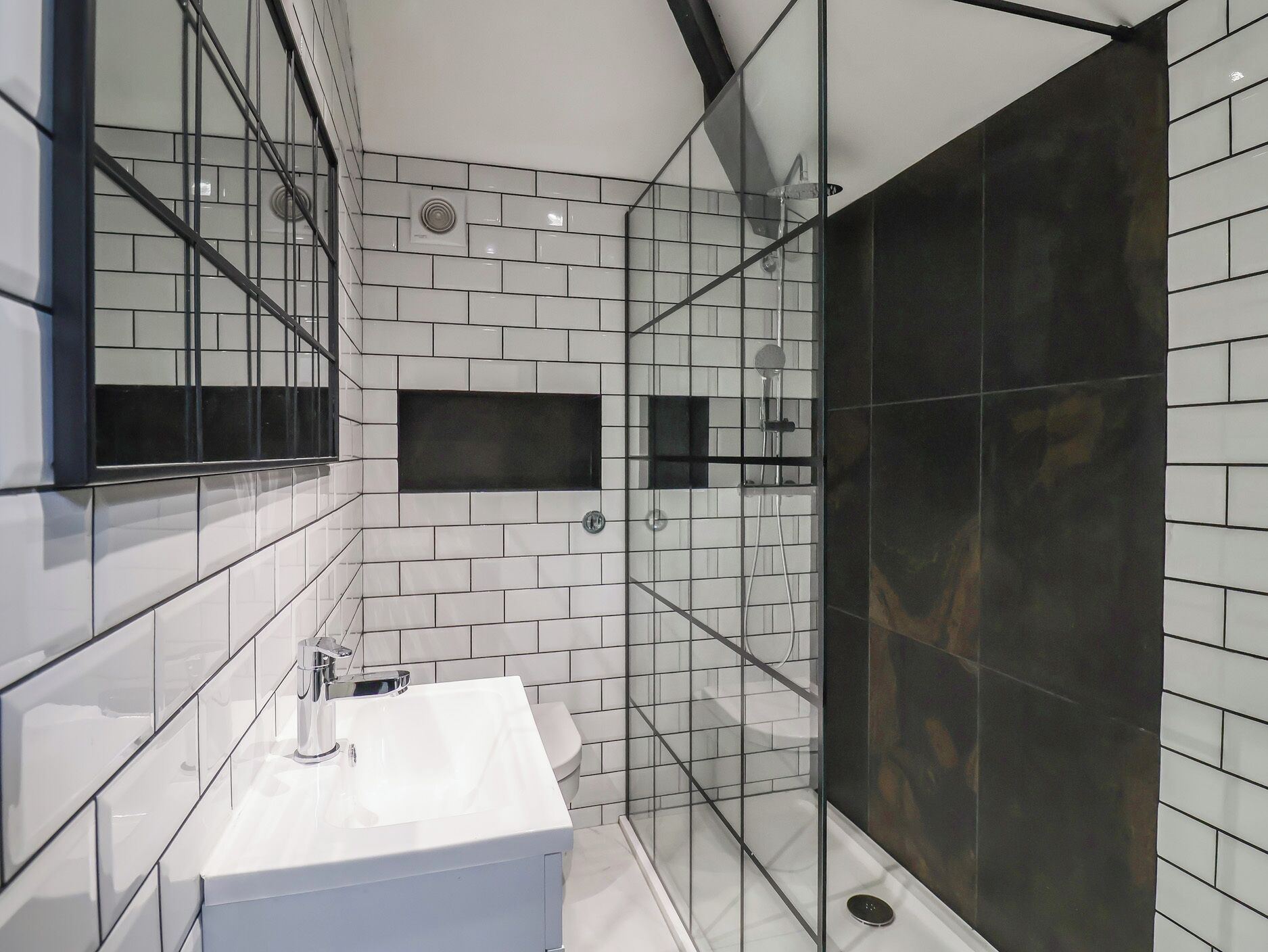 A modern bathroom with a white sink, a glass-enclosed shower, and a large mirror.