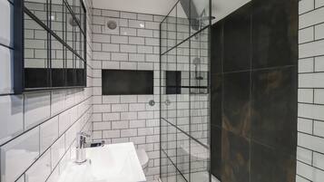 A modern bathroom with a white sink, a glass-enclosed shower, and a large mirror.