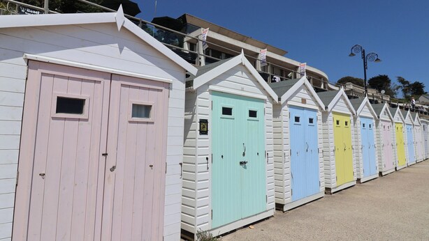 A row of colorful beach huts with a white roof and a balcony, each with a small window and a door. - Drake's Hideaway (Lyme Regis)