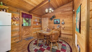 A wooden cabin interior with a dining table, chairs, a refrigerator, and a chandelier.