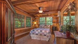 A cozy log cabin bedroom with a bed, a dresser, a nightstand, and a ceiling fan.