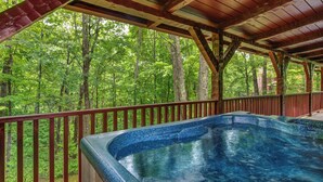 A hot tub with a wooden deck and a view of a forest.