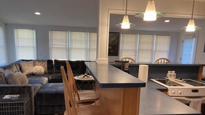 Una sala moderna con un sofá gris oscuro, sillas de madera, una zona de cocina con estufa y una mesa de comedor.