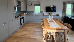 Une cuisine spacieuse avec des meubles de couleur grise, une table à manger en bois et un téléviseur fixé au mur.