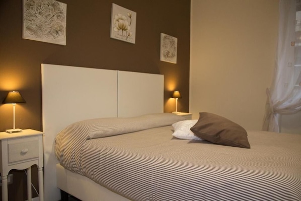 Una cama bien hecha con ropa de cama a rayas, dos lámparas de noche y cuadros en la pared.